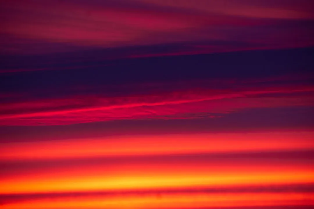 a red and orange sky with a plane in the distance