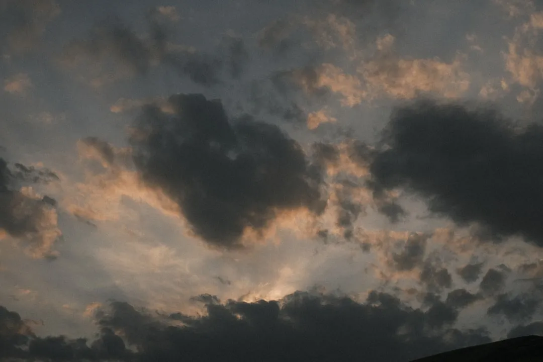 a plane flying through a cloudy sky at sunset