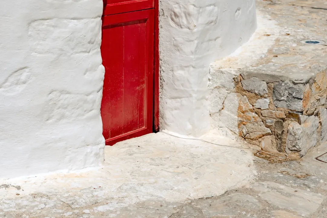 a red door on a white building next to a stone wall