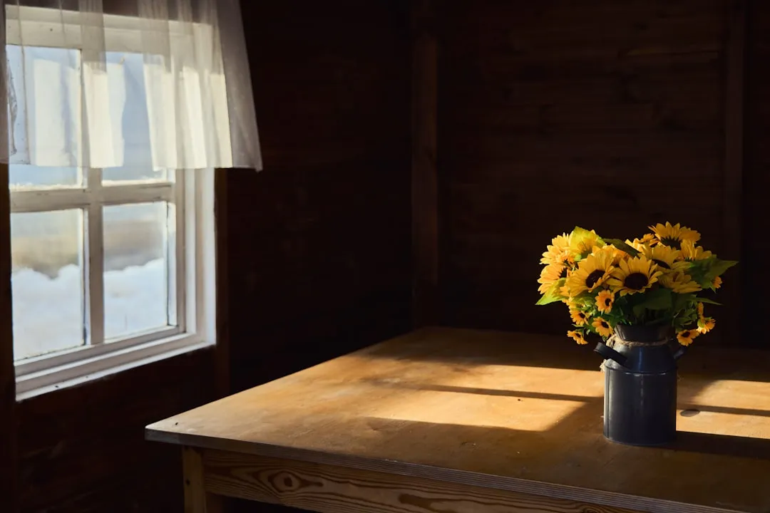 Sunflowers sit on a wooden table by the window