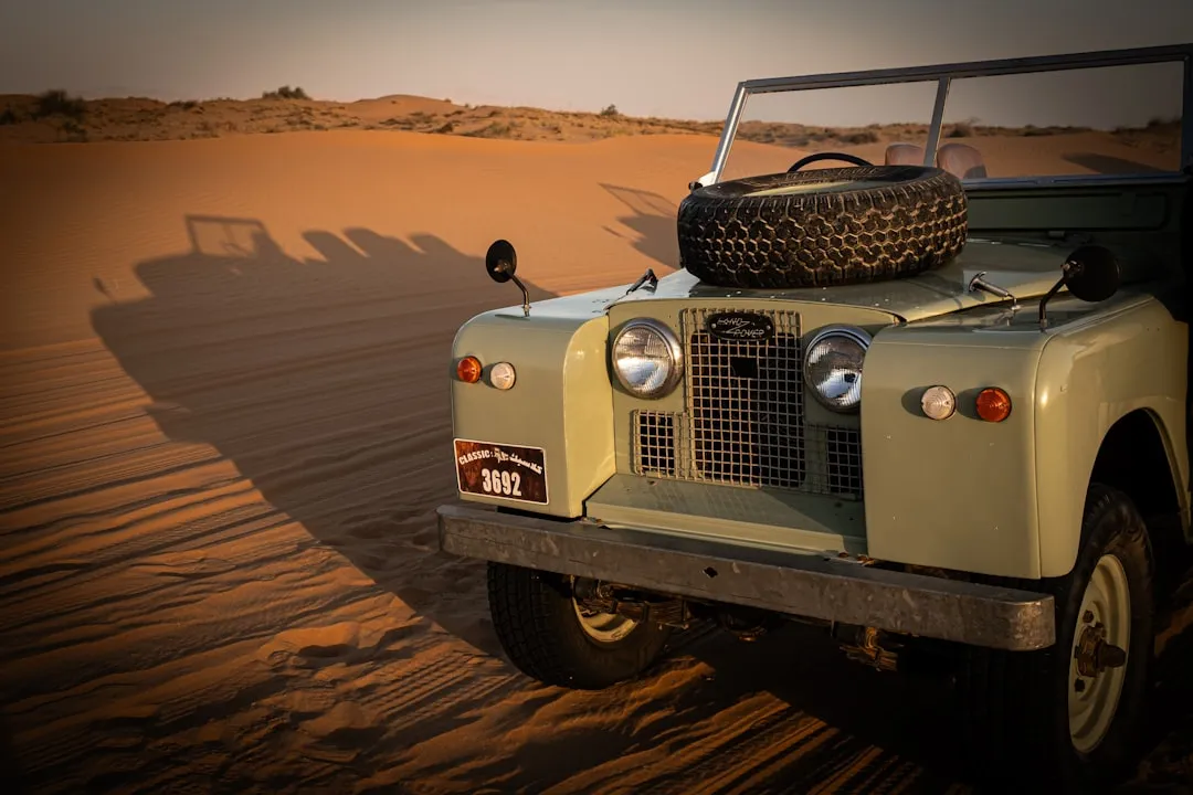 Vintage land rover parked on a sandy desert dune.