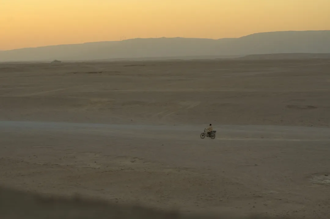 A lone person rides a vehicle across a vast desert.