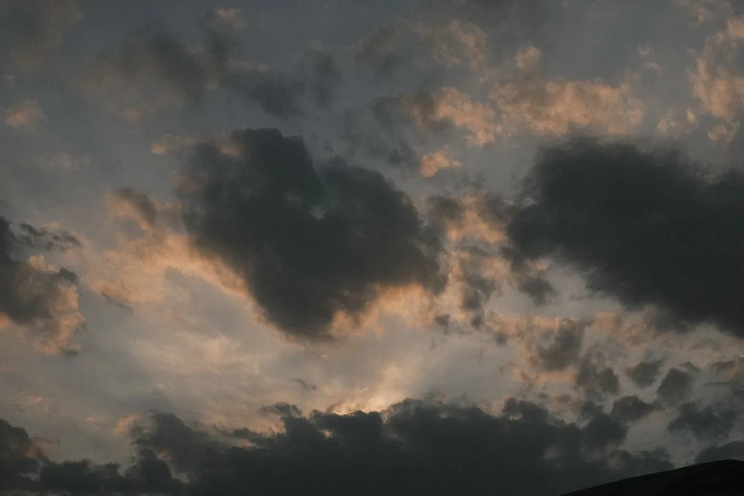 a plane flying through a cloudy sky at sunset